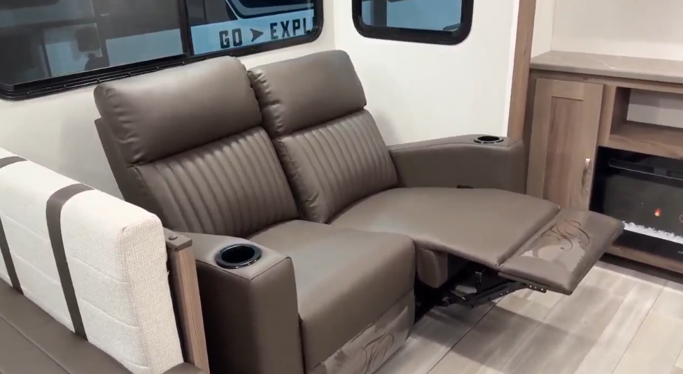 Luxurious recliner seating in the GO Explore travel trailer, featuring plush brown leather upholstery with built-in cup holders. Positioned near large windows for natural light, this comfortable seating area offers relaxation and convenience, ideal for family trips and cozy evenings indoors.