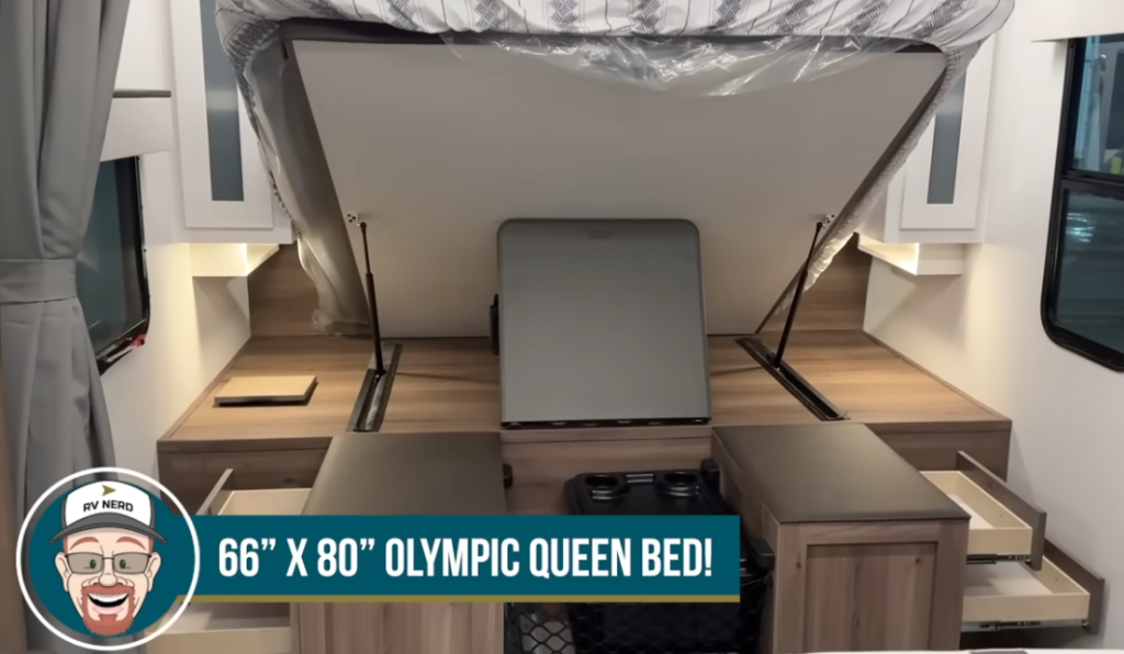 Bedroom area in the GO Explore RV featuring a 66" x 80" Olympic Queen bed with a lift-up design, providing ample storage underneath. The space is enhanced with wood-tone countertops, bedside cabinets, and built-in drawers, offering functionality and comfort for travelers.