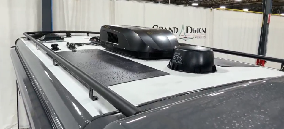 View of the roof of the Lineage luxury motorhome showing its integrated equipment and features. The roof is primarily white with black equipment mounted on top. Visible components include what appears to be an air conditioning unit or climate control system (the rectangular black box), a satellite or WiFi dome labeled with "5G" and "KING", roof rails or tracks along the edges, and possibly solar panels or non-slip walking surfaces (the dark rectangular area). 