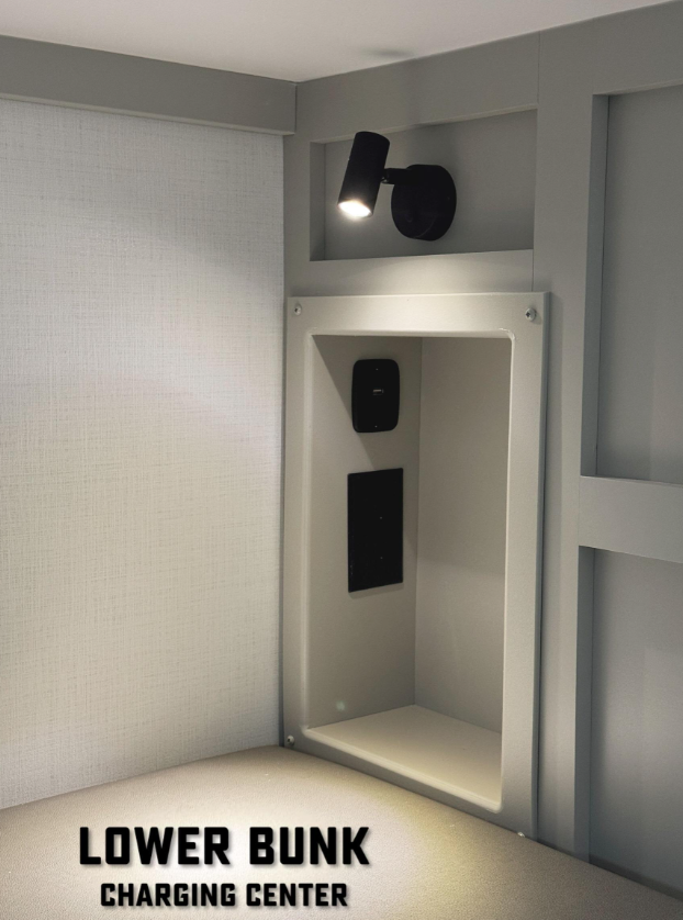 Lower bunk charging center in a Brinkley RV, featuring a built-in cubby with USB and power outlets, a focused overhead reading light, and modern wall paneling for a sleek, functional sleeping space.