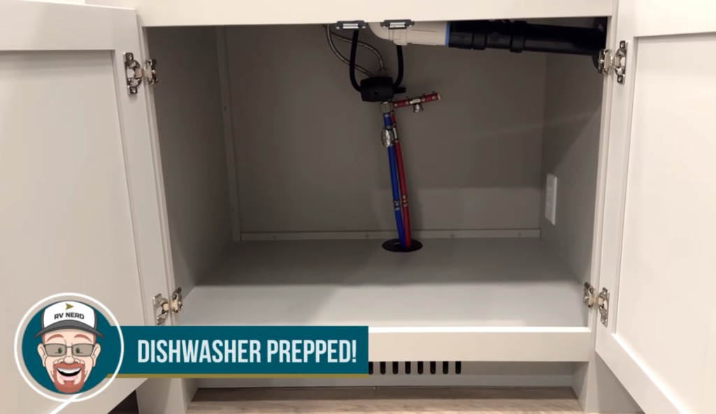  Open lower kitchen cabinet in a Brinkley RV showcasing dishwasher prep with visible plumbing and electrical connections, highlighted by a "Dishwasher Prepped!" banner featuring RV Nerd branding in the bottom left corner.
