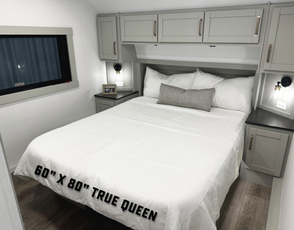 Brinkley RV bedroom featuring a 60" x 80" true queen bed with overhead cabinets, dual nightstands, modern sconces, and under-bed storage, showcasing a bright, residential design.