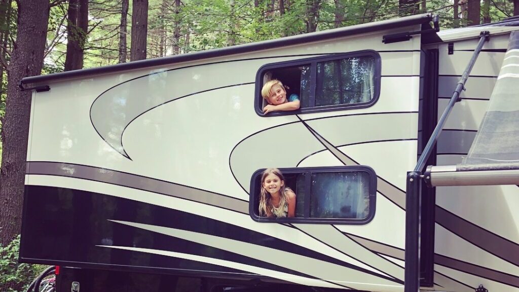 2 smiling kids hanging out camper windows