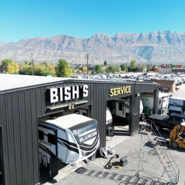 Exterior view of Bish’s RV Service Center with RVs parked inside service bays, mountains in the background, and rows of RVs lined up across the lot.