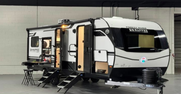 Forest River R-Pod Unmapped travel trailer displayed indoors with slide-outs extended and exterior kitchen open, featuring a modern white and black design.