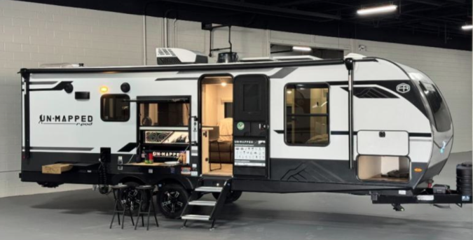 A Forest River R-Pod Unmapped travel trailer with a modern white and black exterior, extended entry steps, large front window, and dual axles, displayed indoors under bright lighting.