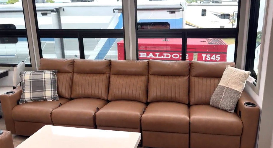 Luxurious brown leather reclining sofa with cupholders inside the Axiom Imperium 12900 fifth wheel RV, placed in front of large panoramic windows for natural light.