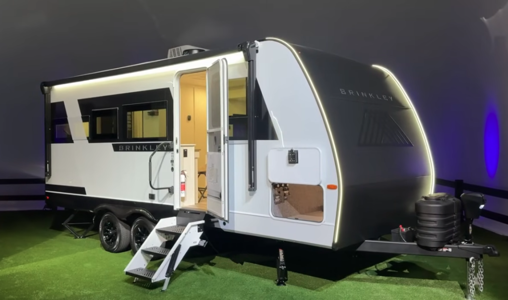 2026 Brinkley travel trailer with aerodynamic front cap, LED accent lighting, dual axles, and entry steps extended for display.