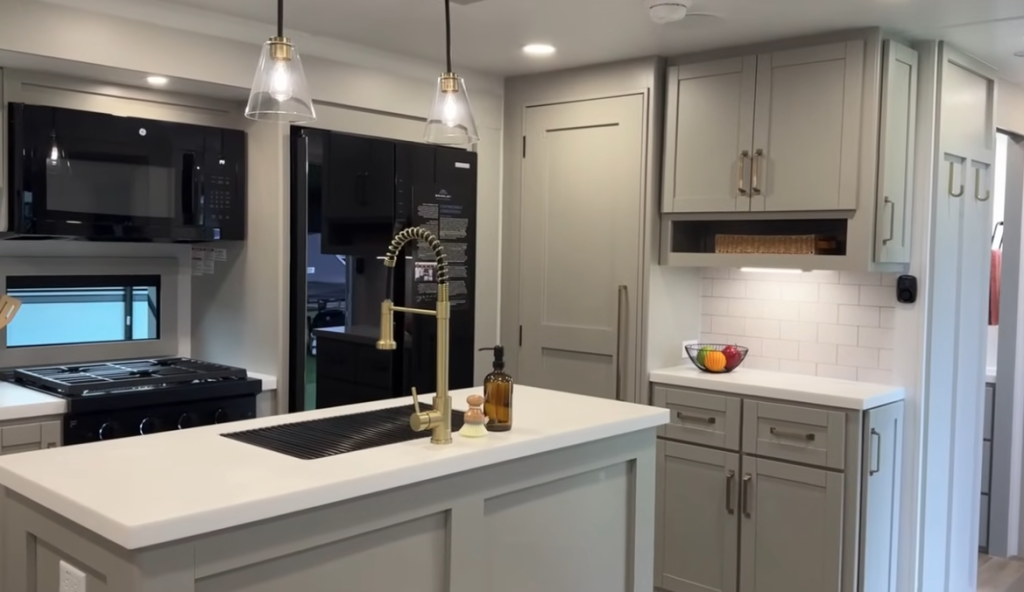 Brinkley RV luxury kitchen with center island, modern faucet, residential refrigerator, overhead cabinets, and stylish pendant lighting.