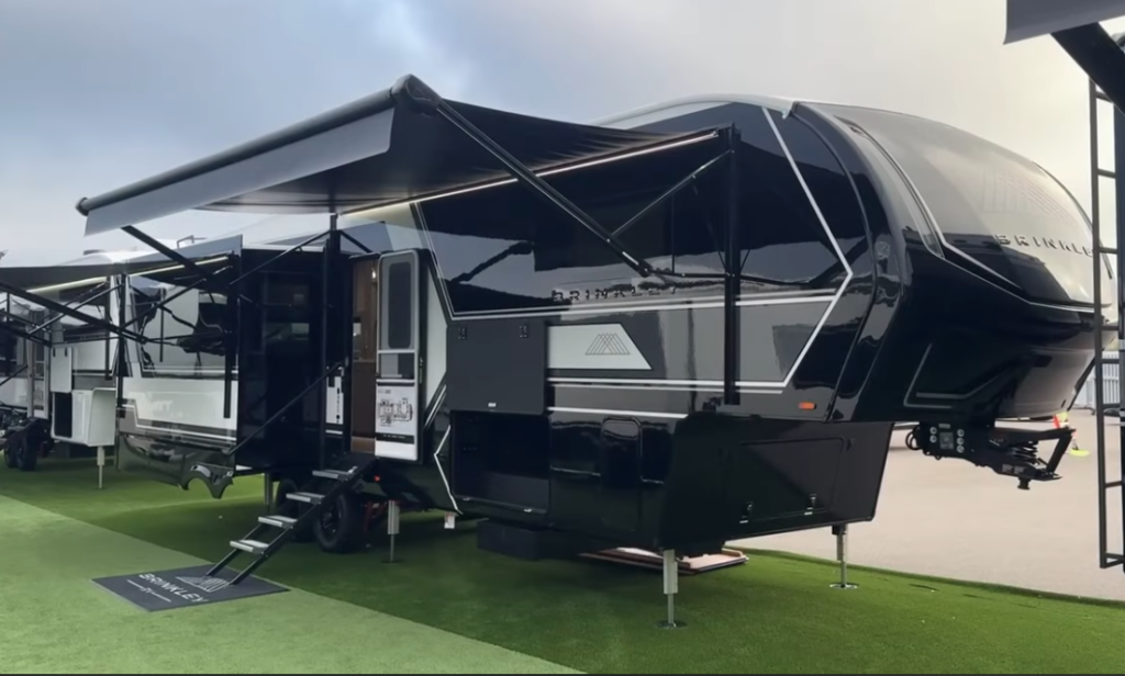2026 Brinkley luxury fifth wheel RV with awning extended, featuring sleek black and gold exterior design and modern full-profile front cap.