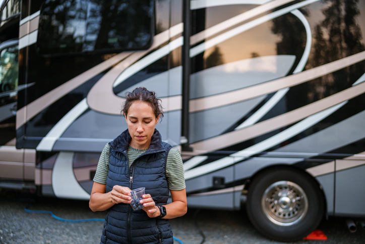 woman stands outside her RV in a campground and eats blueberries from a plastic cup.