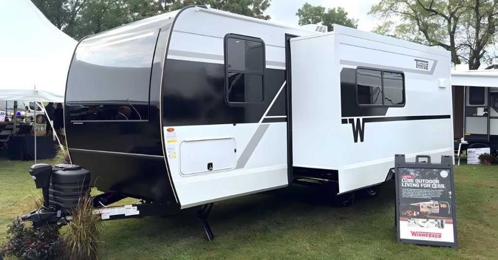 2026 Winnebago Thrive 22MLS travel trailer with bold black-and-white exterior, single slide-out, and aerodynamic front profile on display outdoors at an RV show.