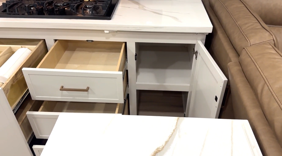 Open kitchen storage in the Brinkley Model I 280 showing dovetail drawers, a pull-out paper towel and trash bin system, and lower cabinet space beneath the solid-surface countertop and three-burner cooktop. The design highlights Brinkley’s practical organization and residential-quality construction.