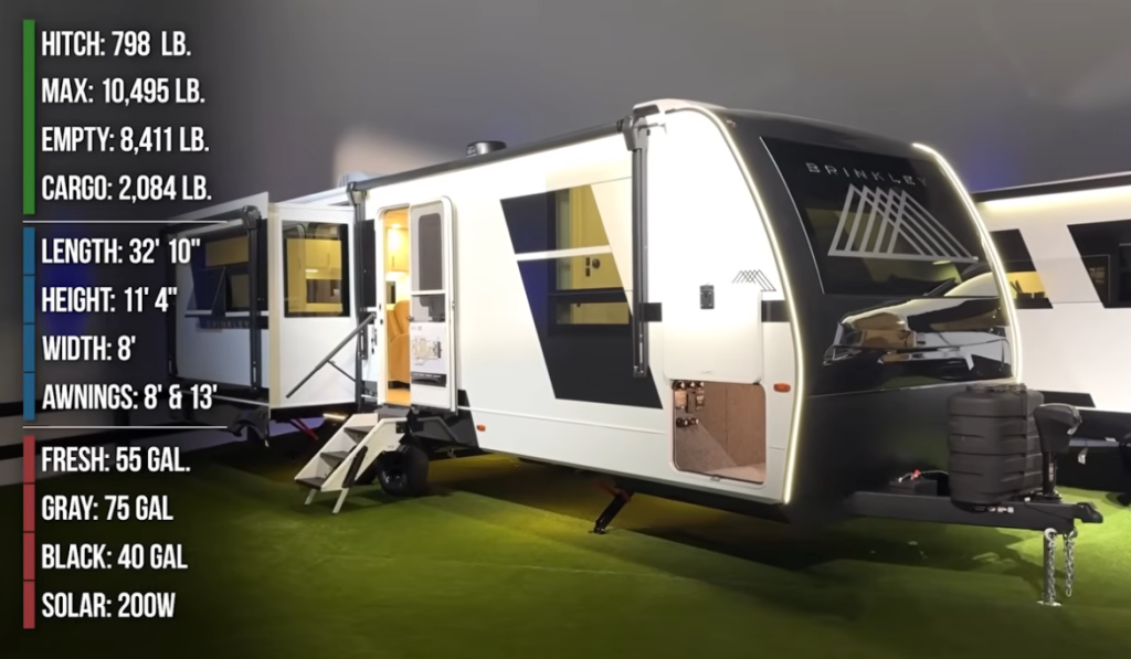 Exterior view of the Brinkley Model I 280 travel trailer with LED accent lighting and dual slide-outs. On-screen specs list key details: hitch weight 798 lbs, GVWR 10,495 lbs, dry weight 8,411 lbs, cargo capacity 2,084 lbs, length 32'10", height 11'4", width 8', dual awnings (8' and 13'), 55-gallon fresh tank, 75-gallon gray tank, 40-gallon black tank, and 200W solar.