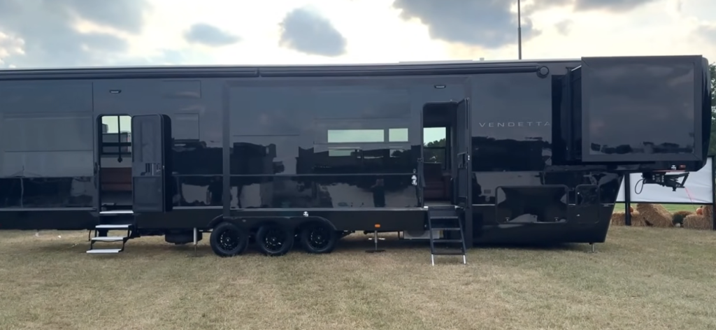 Side exterior view of the 2026 Axiom Vendetta fifth wheel RV featuring a sleek all-black design, triple axles, multiple entry doors, and flush-mounted windows for a high-end modern appearance.
