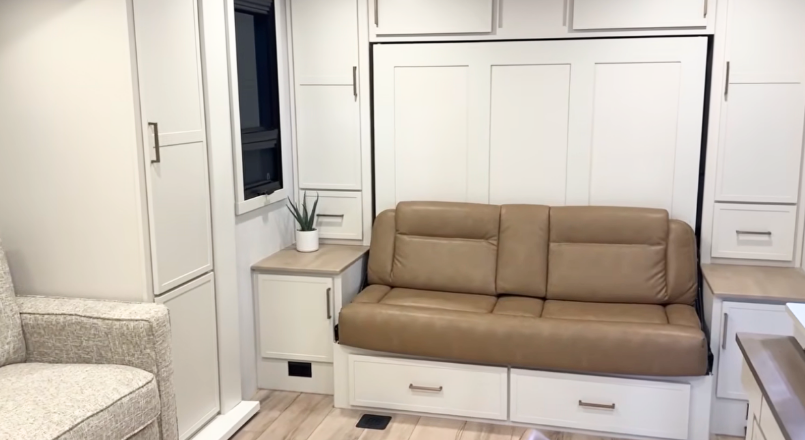 Brinkley Model Ix 20X interior showing tan leather Murphy sofa with surrounding storage cabinets, light modern cabinetry, and soft neutral décor inside the compact travel trailer.