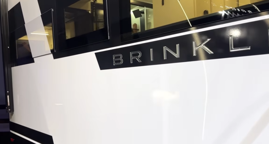 Close-up of Brinkley Model Ix 20X exterior showing painted aluminum sidewall with glossy black trim and bold Brinkley logo for a sleek modern RV design.