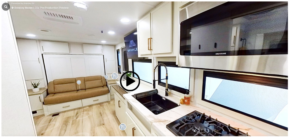 Brinkley Model Ix 20X interior view showing modern kitchen with marble-look countertops, stainless microwave, deep farmhouse sink, and Murphy sofa bed across from large panoramic windows.