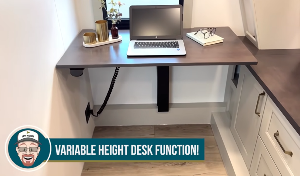Adjustable height desk inside the 2026 Axiom Imperium I3800 fifth wheel RV featuring an electric lift workspace with laptop, modern cabinetry, and wood-look flooring—ideal for remote work or creative use on the road.