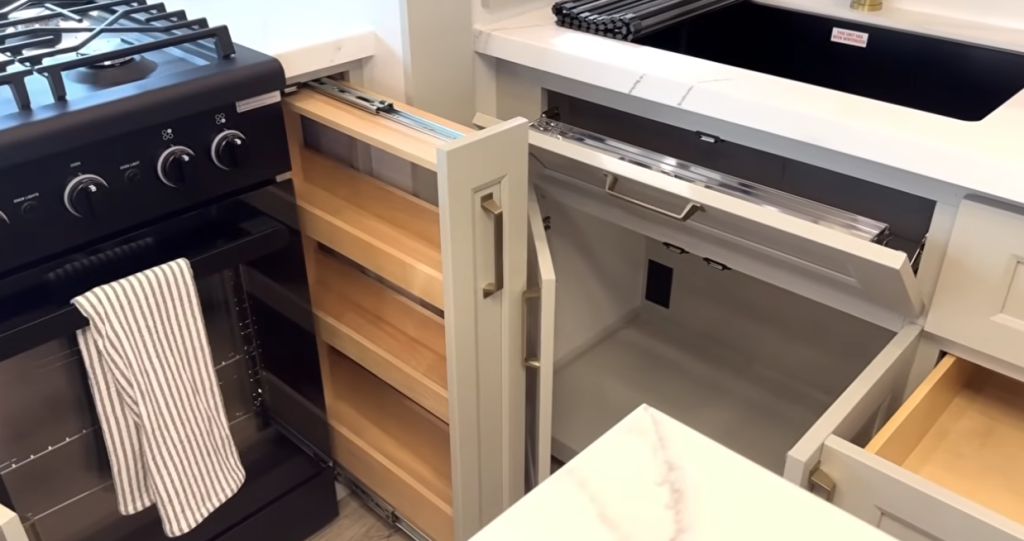 Brinkley Model G Series RV kitchen with pull-out spice rack beside a black gas range, tilt-out sink tray, and deep storage drawers, highlighting smart space-saving design and premium functionality.