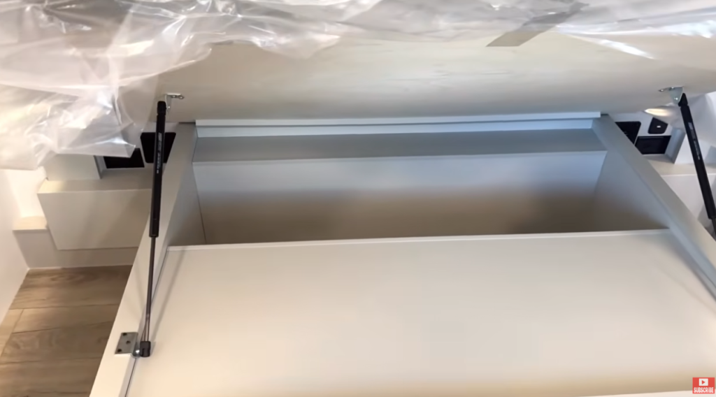 Brinkley Model G Series RV bedroom under-bed storage with gas strut lift system, providing hidden storage space for bedding, gear, or seasonal items beneath the residential king mattress.