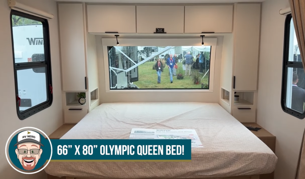 2026 Winnebago Thrive 22MLS bedroom featuring a 66x80 Olympic queen bed, large panoramic front window, modern cabinetry, and built-in bedside storage with reading lights.