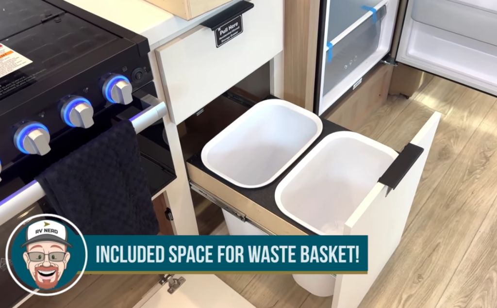2026 Winnebago Thrive 22MLS kitchen with built-in pull-out waste bin drawer featuring dual trash containers beside the stove, showcasing practical and space-saving design.