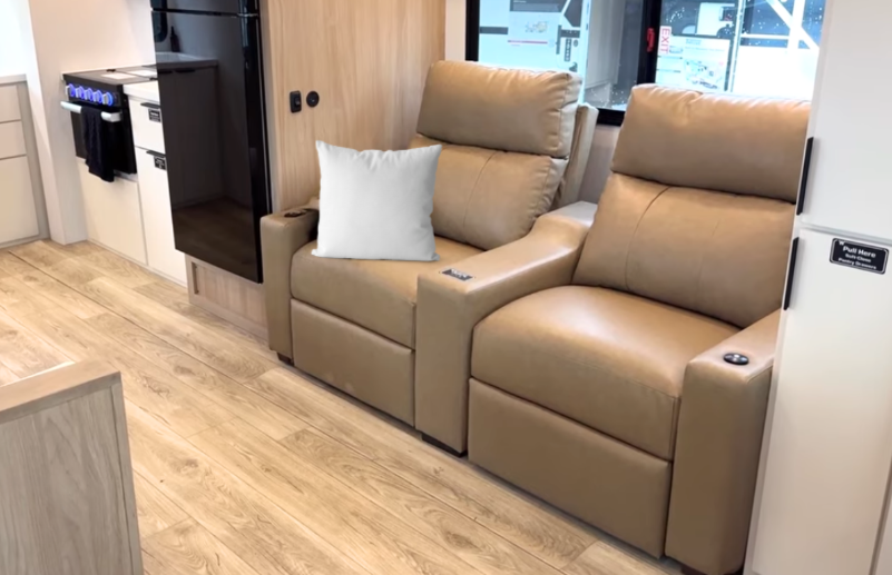 2026 Winnebago Thrive 22MLS interior featuring dual tan leather recliners with cup holders, modern wood-look flooring, and a contemporary kitchen layout with sleek cabinetry and appliances.