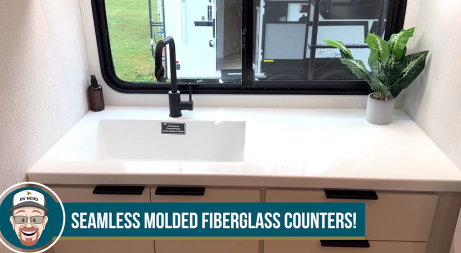 2026 Winnebago Thrive 22MLS kitchen with seamless molded fiberglass countertop, deep integrated sink, black faucet, and large window providing natural light and outdoor views.