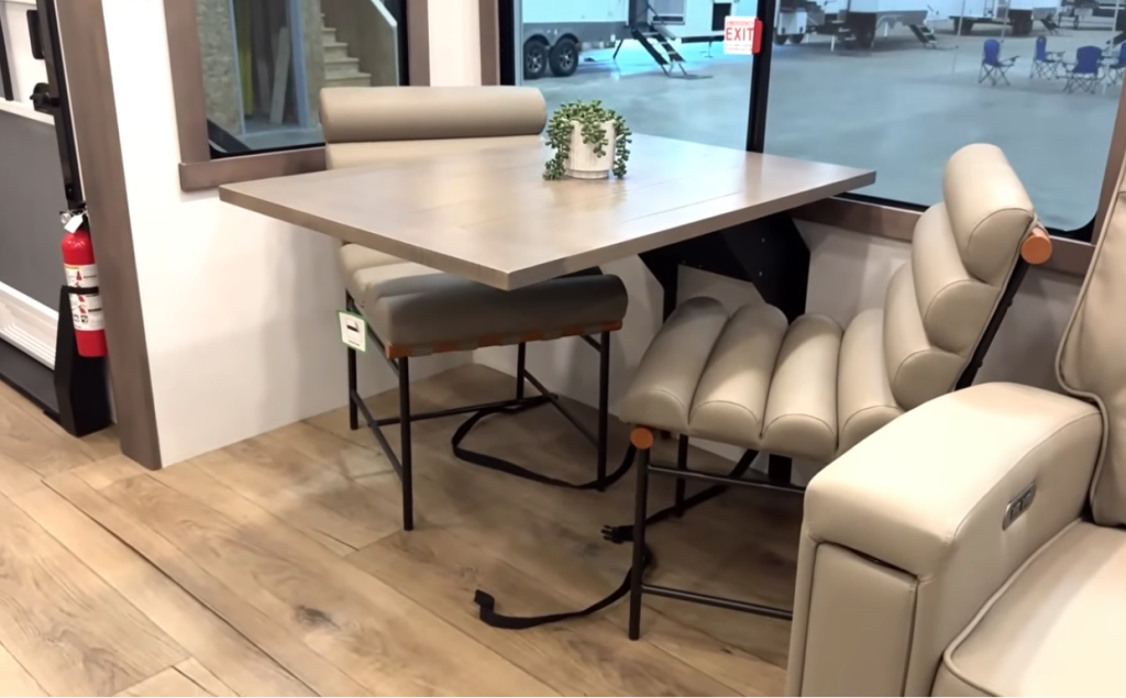 Alliance Paradigm fifth wheel dinette area with modern wood table, two padded chairs, and a large window for natural light, featuring soft neutral tones and stylish RV dining design.