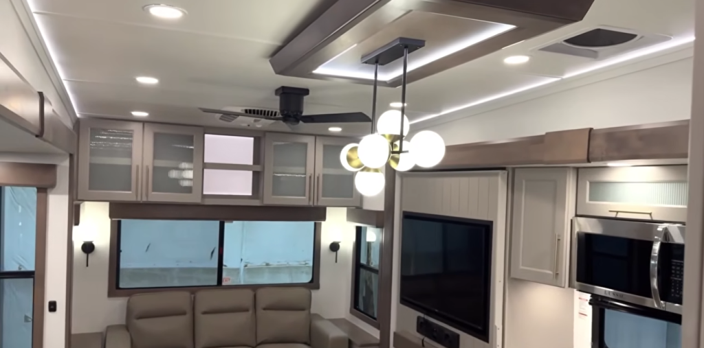 lliance Paradigm fifth wheel interior ceiling view showing modern pendant lighting, recessed LED lights, ceiling fan, and overhead cabinetry above the living room and entertainment area.