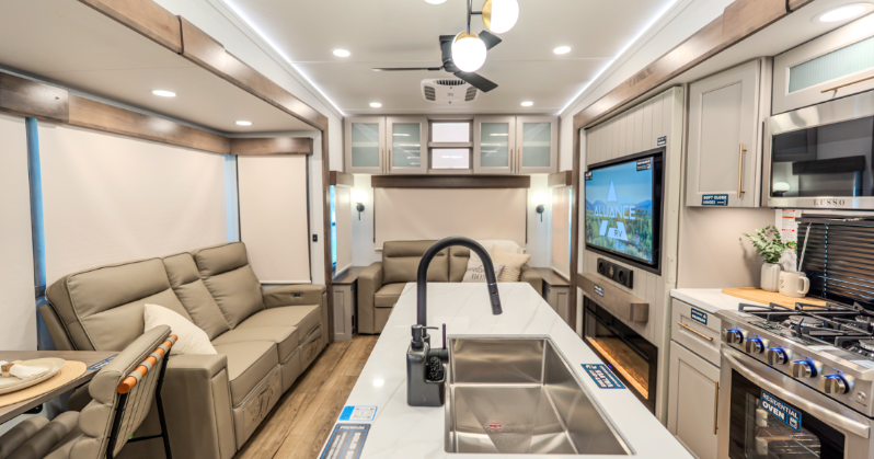 Alliance Paradigm fifth wheel interior featuring a modern kitchen island with dual sink, stainless steel appliances, and spacious living area with theater seating, tri-fold sofa, and large entertainment center.