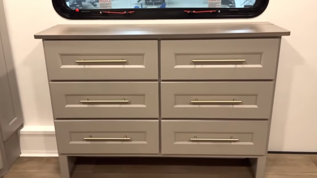 Six-drawer dresser in the Alliance Paradigm fifth wheel bedroom, featuring modern gold hardware and a wood-tone countertop beneath a large window.