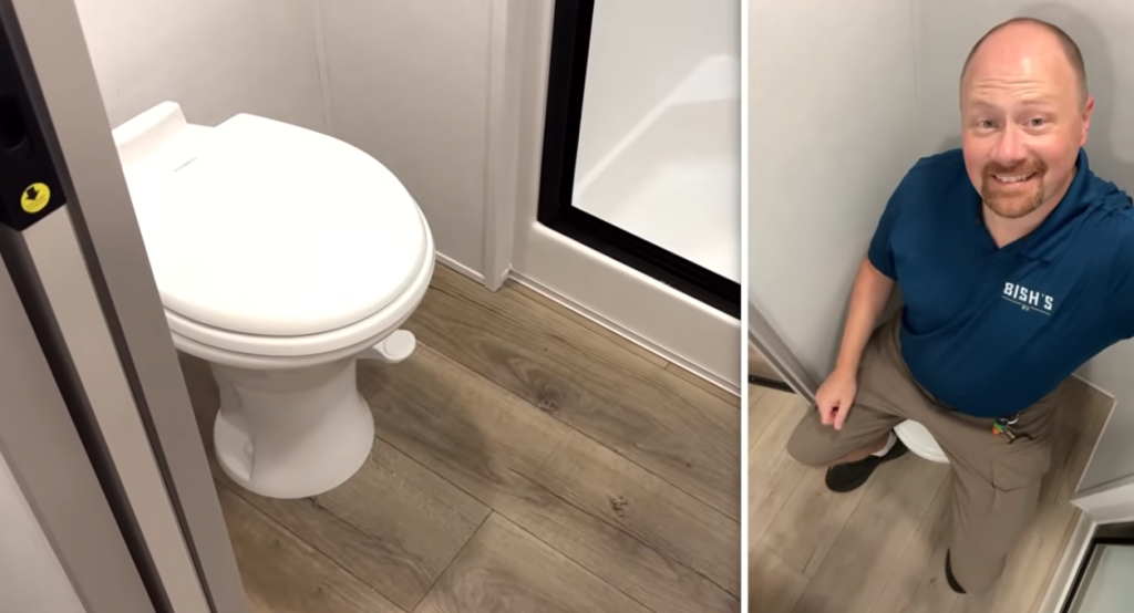 Alliance Paradigm fifth wheel bathroom with porcelain foot-flush toilet, wood-look flooring, and spacious layout next to the glass shower enclosure.