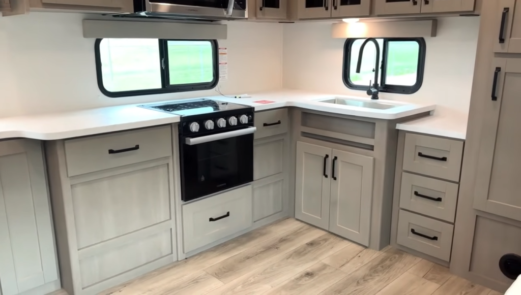 2026 Grand Design Reflection 150 270BN kitchen with U-shaped counters, gas range, deep sink with black faucet, and light cabinetry offering ample storage and workspace.