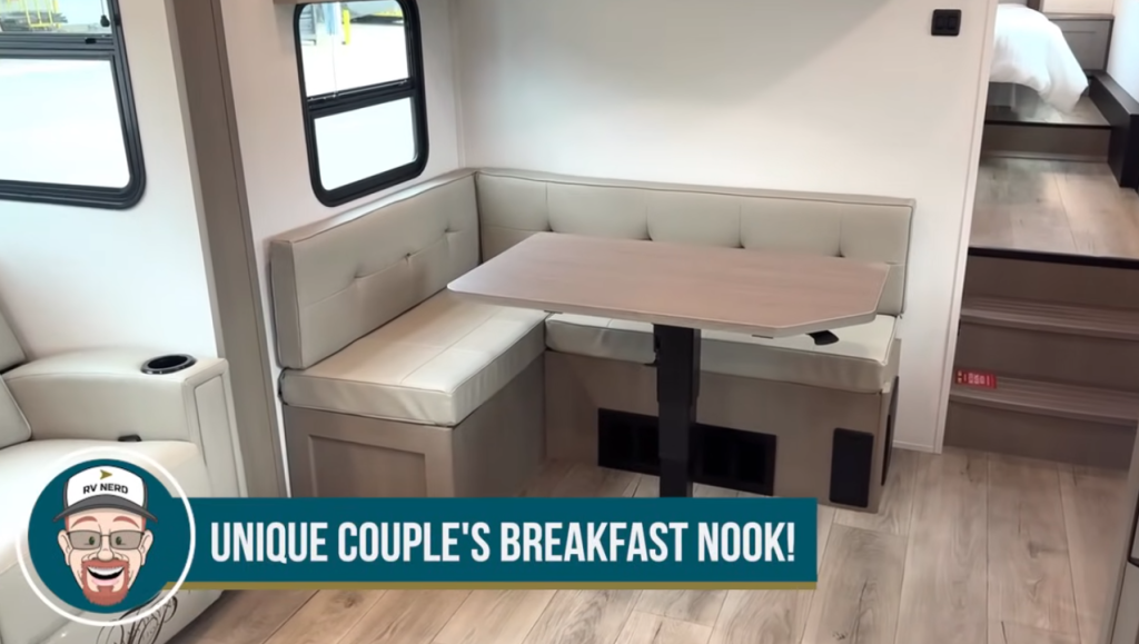 2026 Grand Design Reflection 150 270BN interior showing the unique couple’s breakfast nook with cushioned seating, modern dining table, and steps leading to the bedroom suite.