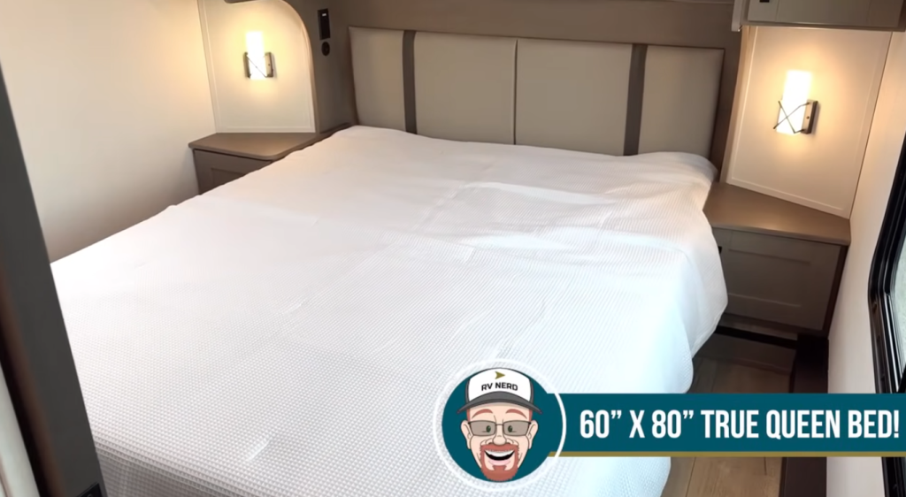 2026 Grand Design Reflection 150 270BN bedroom featuring a 60x80 true queen bed, dual nightstands, overhead storage cabinets, and soft reading lights for a comfortable retreat.