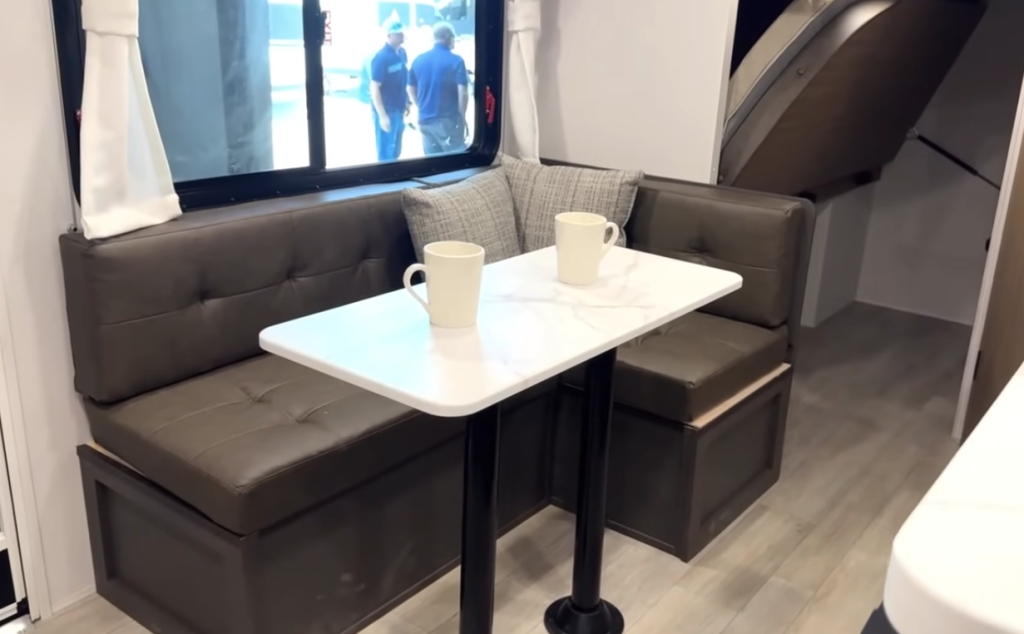 Forest River Wildwood FSX travel trailer interior dinette with brown tufted seating, white marble-look table, and convertible bed storage design for compact dining space.