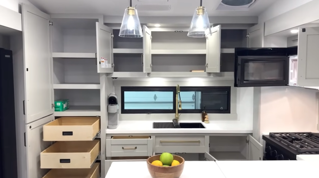 Brinkley Model Z fifth wheel kitchen with open cabinetry, pull-out pantry drawers, black farmhouse sink, and pendant lighting highlighting spacious storage and modern RV kitchen design.