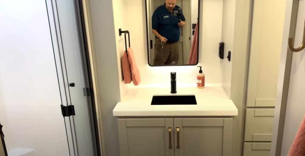 Brinkley Model Z RV bathroom vanity with modern square sink, matte black faucet, backlit mirror, and soft gold hardware, blending residential luxury with practical storage design.