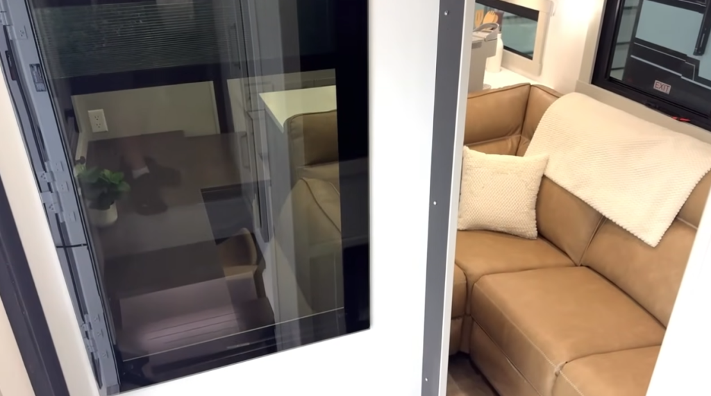 Brinkley Model Z rear living area featuring a tan leather sectional sofa with accent pillows, adjacent to a sliding glass patio door and workspace with modern finishes and natural light.