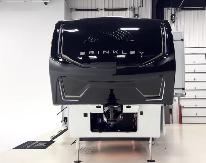 Front view of the Brinkley Model Z fifth wheel featuring a sleek aerodynamic front cap with metallic black finish, integrated LED accent lights, and bold BRINKLEY logo design.