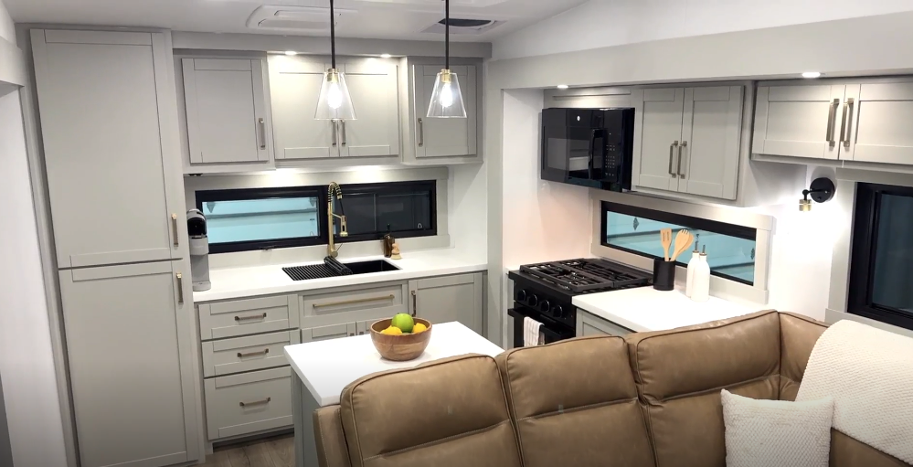 Brinkley Model Z fifth wheel kitchen featuring modern cabinetry, dual windows for natural light, pendant lighting, stainless steel appliances, and a central island with fruit bowl décor for a residential feel.