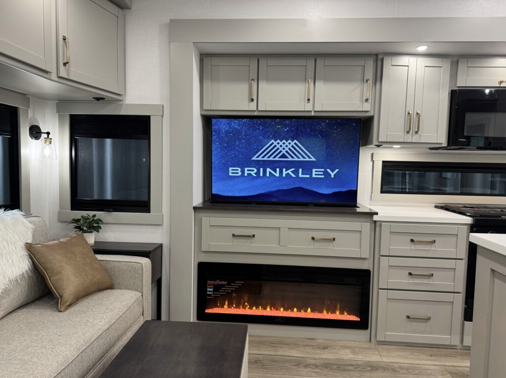 Brinkley Model Z 3600 living area featuring a televator TV with Brinkley logo, electric fireplace, modern cabinetry, and a cozy sofa with accent pillow and wall sconce lighting.