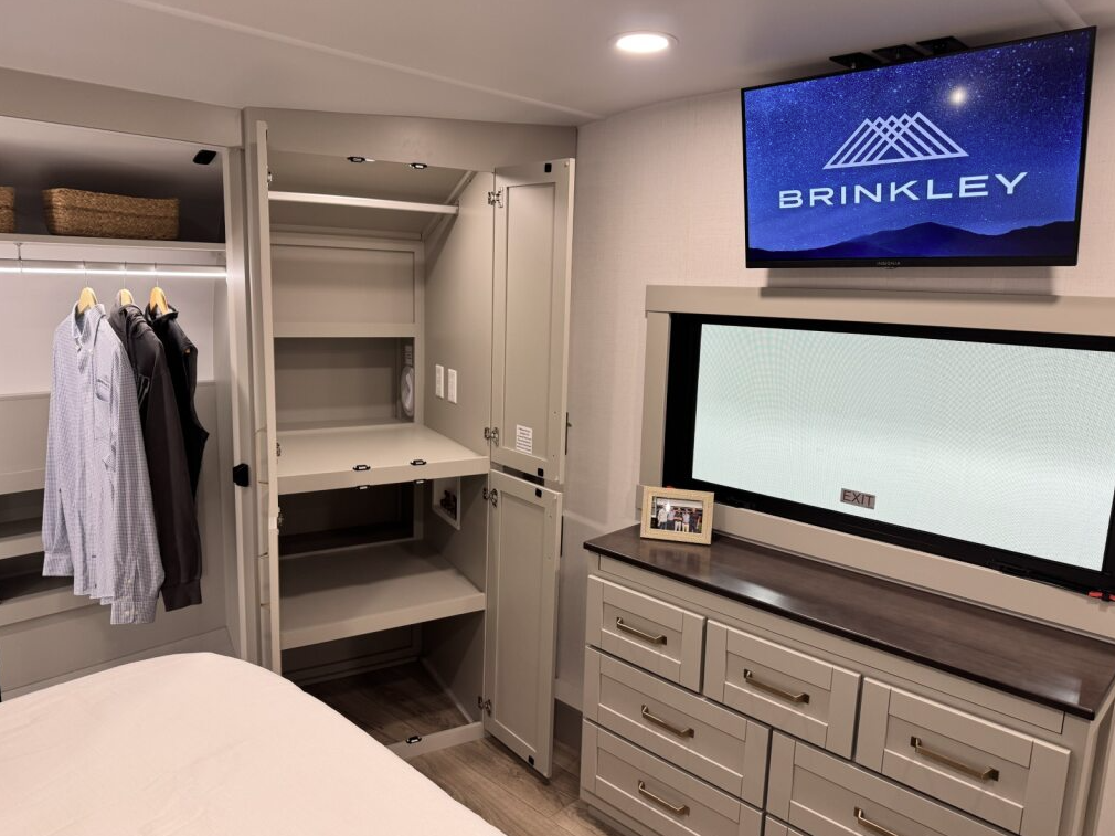 Brinkley Model Z 3600 bedroom wardrobe with open storage compartments, hanging closet, dresser drawers, and TV above a large window showcasing the RV’s spacious and organized design.