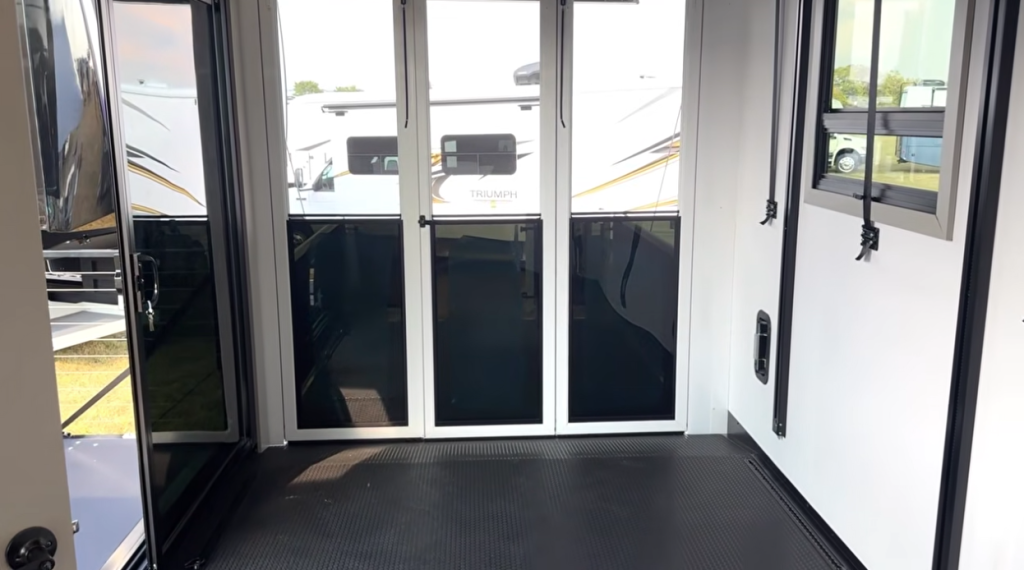 Garage area of the 2026 Axiom Vendetta 4250 fifth wheel toy hauler featuring a clean, open layout with tie-down tracks, large windows, and glass patio doors leading to the rear deck.