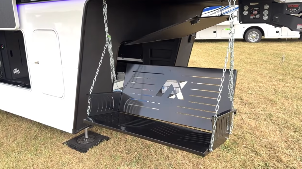 Front storage compartment of the 2026 Axiom Vendetta 4250 fifth wheel featuring a fold-down metal TrailGator swing bar with the Axiom logo, designed for outdoor seating and utility use.