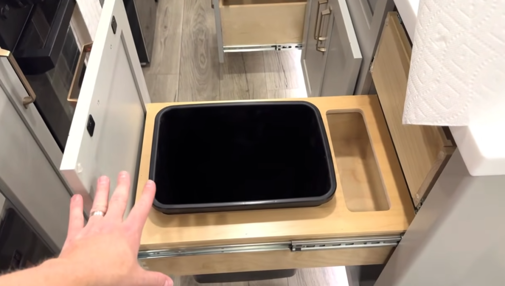 Pull-out RV kitchen trash drawer in the 2026 Brinkley Model Z Air featuring a built-in wastebasket, paper towel holder, and integrated storage tray on soft-close slides.