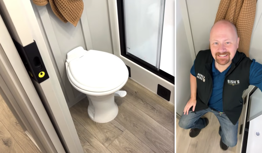 RV bathroom in the 2026 Brinkley Model Z Air showing a porcelain foot-flush toilet, walk-in fiberglass shower, and spacious floor area with Josh the RV Nerd sitting to demonstrate legroom.