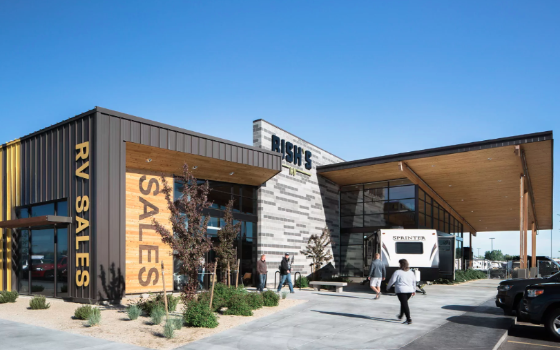 Exterior view of Bish’s RV dealership with modern architecture, RVs on display, and customers walking through the sales lot under a clear blue sky.